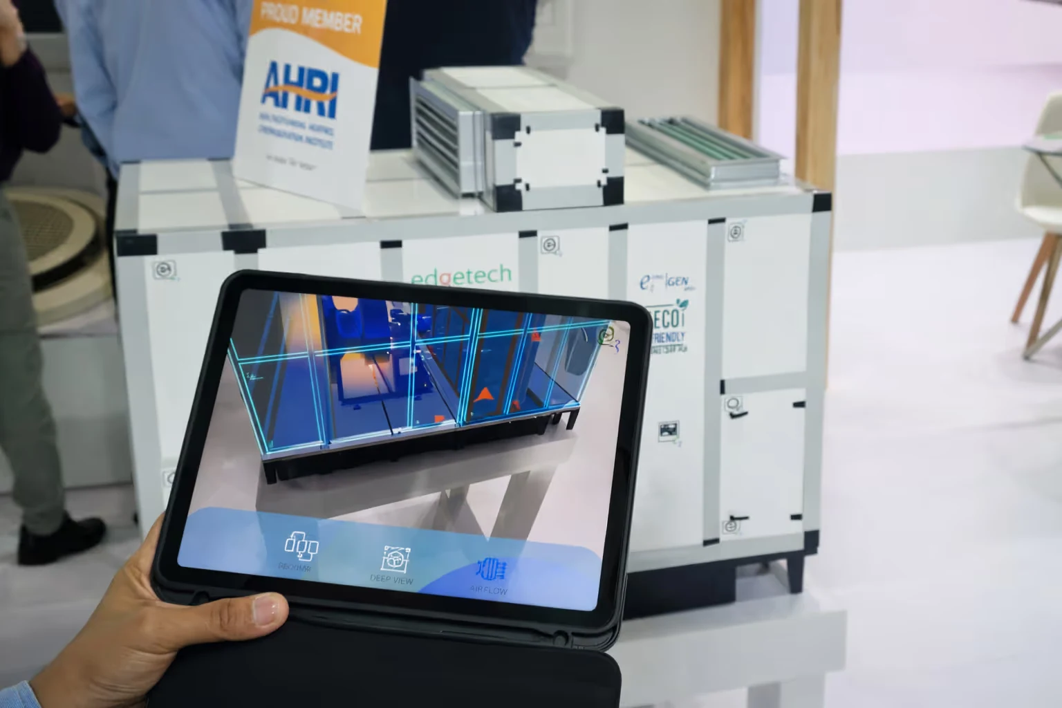 Hand holding a tablet displaying a 3D model with blue grid lines in front of a white industrial equipment unit labeled as eco-friendly and AHRI member.
