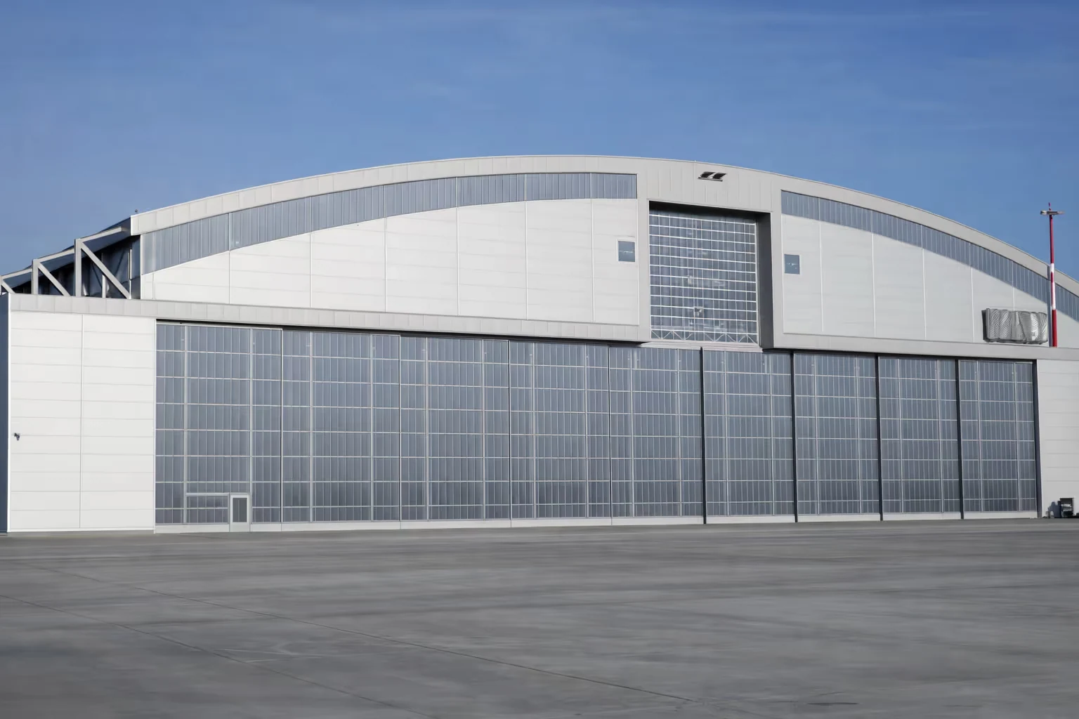 Large modern aircraft hangar with tall segmented glass doors under a clear blue sky.