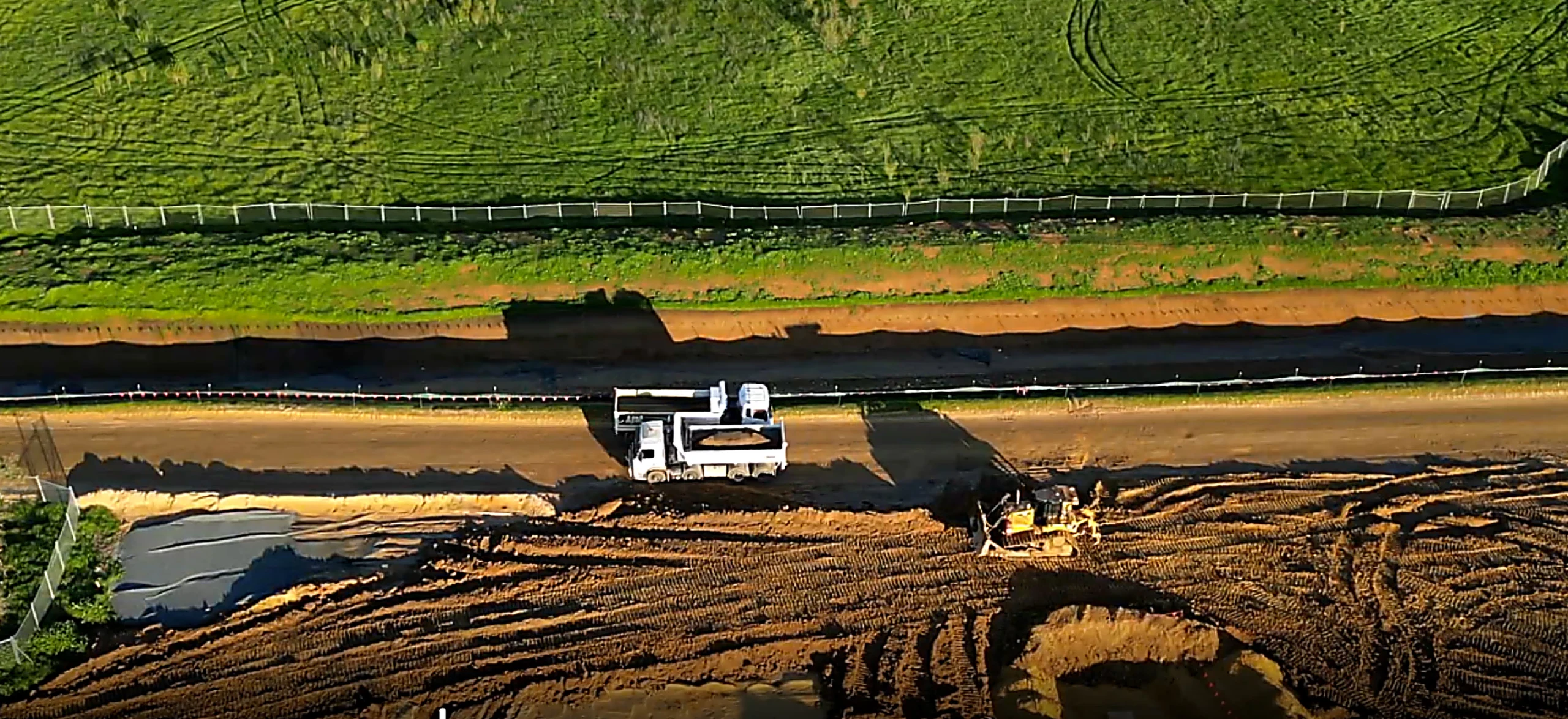 Aerial view of a construction site with a white truck and a bulldozer working on the dirt road next to green grassy land.