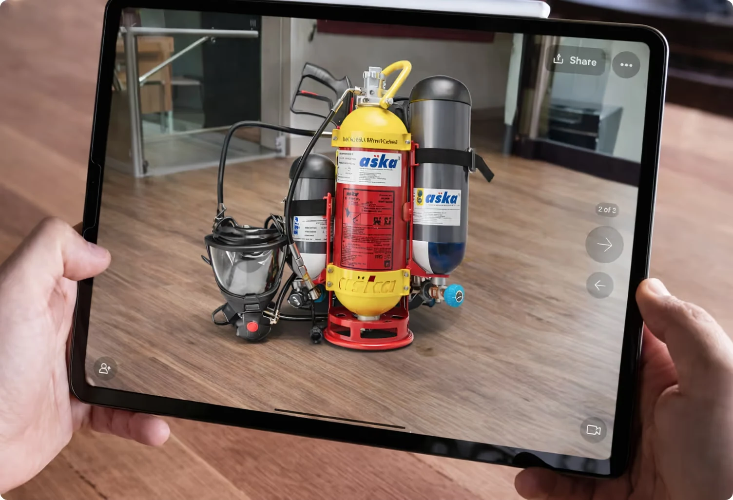 Hands holding a tablet displaying a 3D model of a red and yellow fire safety breathing apparatus with attached gas cylinders and a face mask.