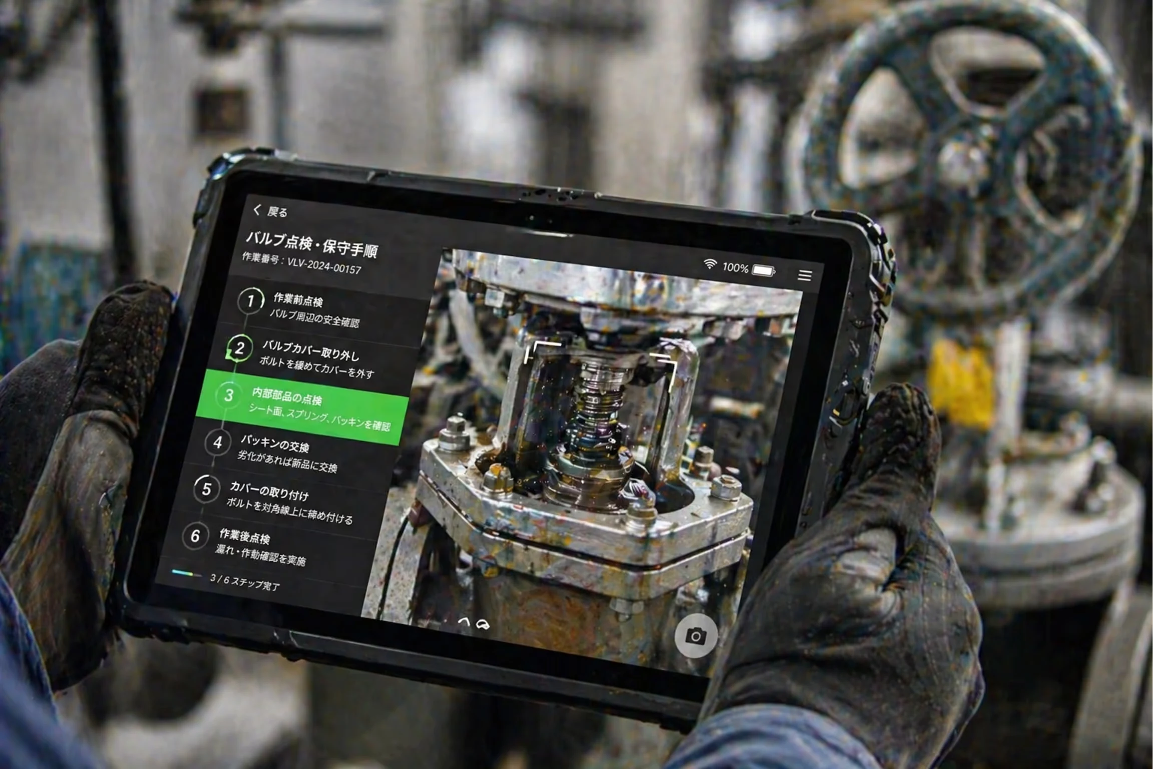 Gloved hands holding a rugged tablet showing detailed Japanese instructions for valve inspection and maintenance, with a close-up image of a valve component on screen.